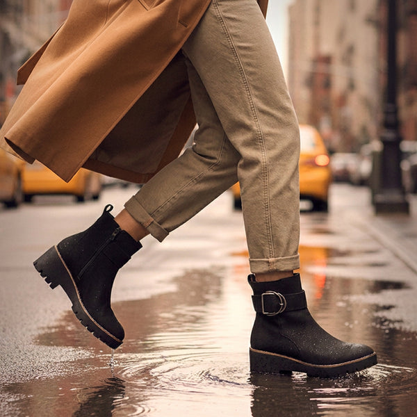 DAGGER A person walking on a wet city street wearing black ankle boots with side buckles, beige pants, and a tan coat. Yellow taxis and blurred buildings are visible in the background. - thumbnail image 2 of 74