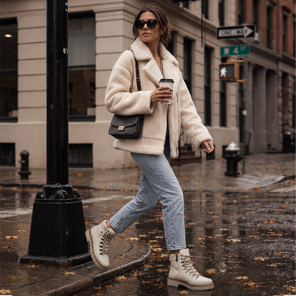 NATASIA A woman walking on a wet city street wearing a cream sherpa fleece jacket, light blue jeans, off-white waterproof lace-up boots, and carrying a black shoulder bag. - thumbnail image 2 of 40